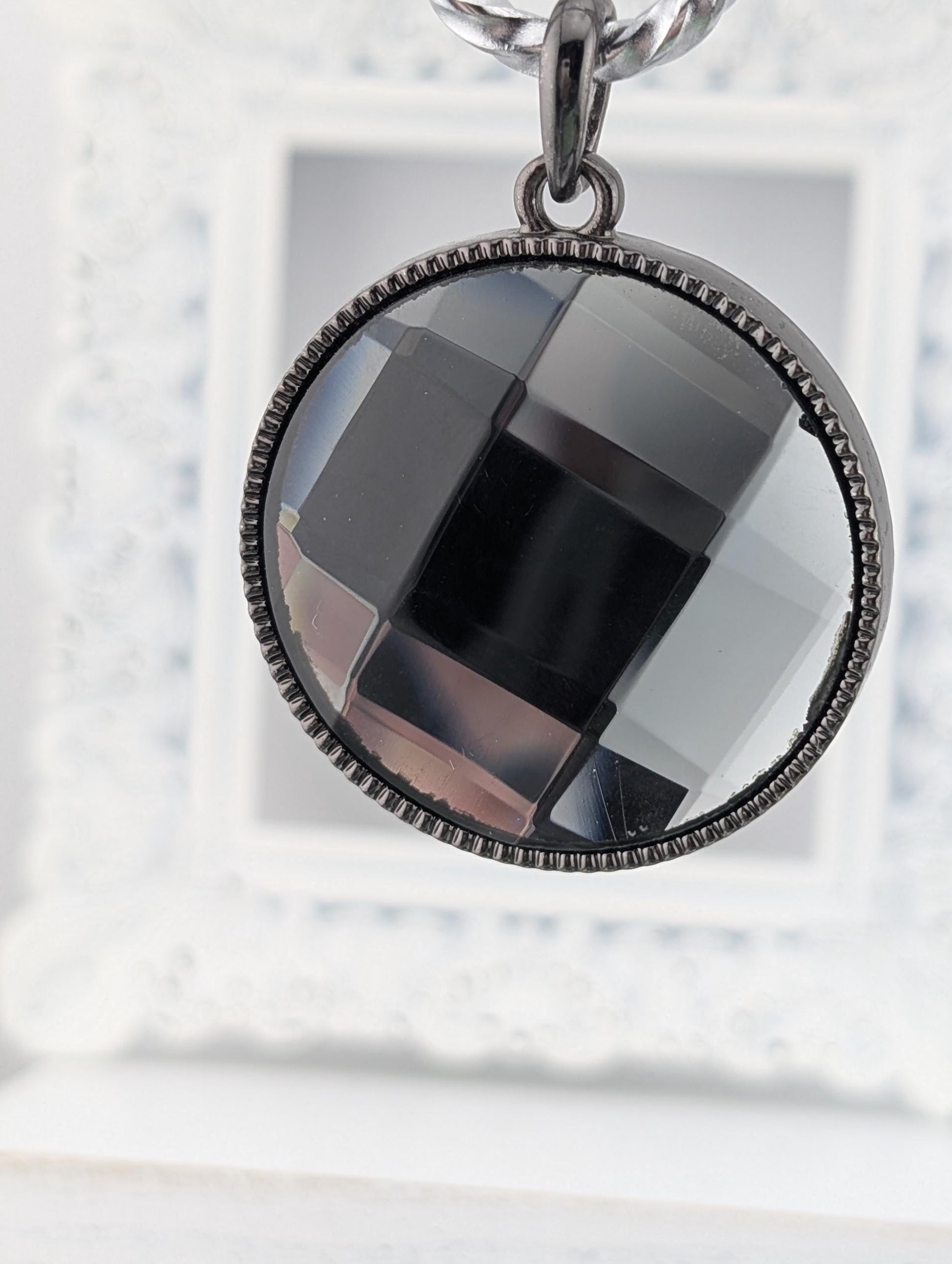 A close-up view of a circular pendant with a black and gray geometric design, hanging from a chain.