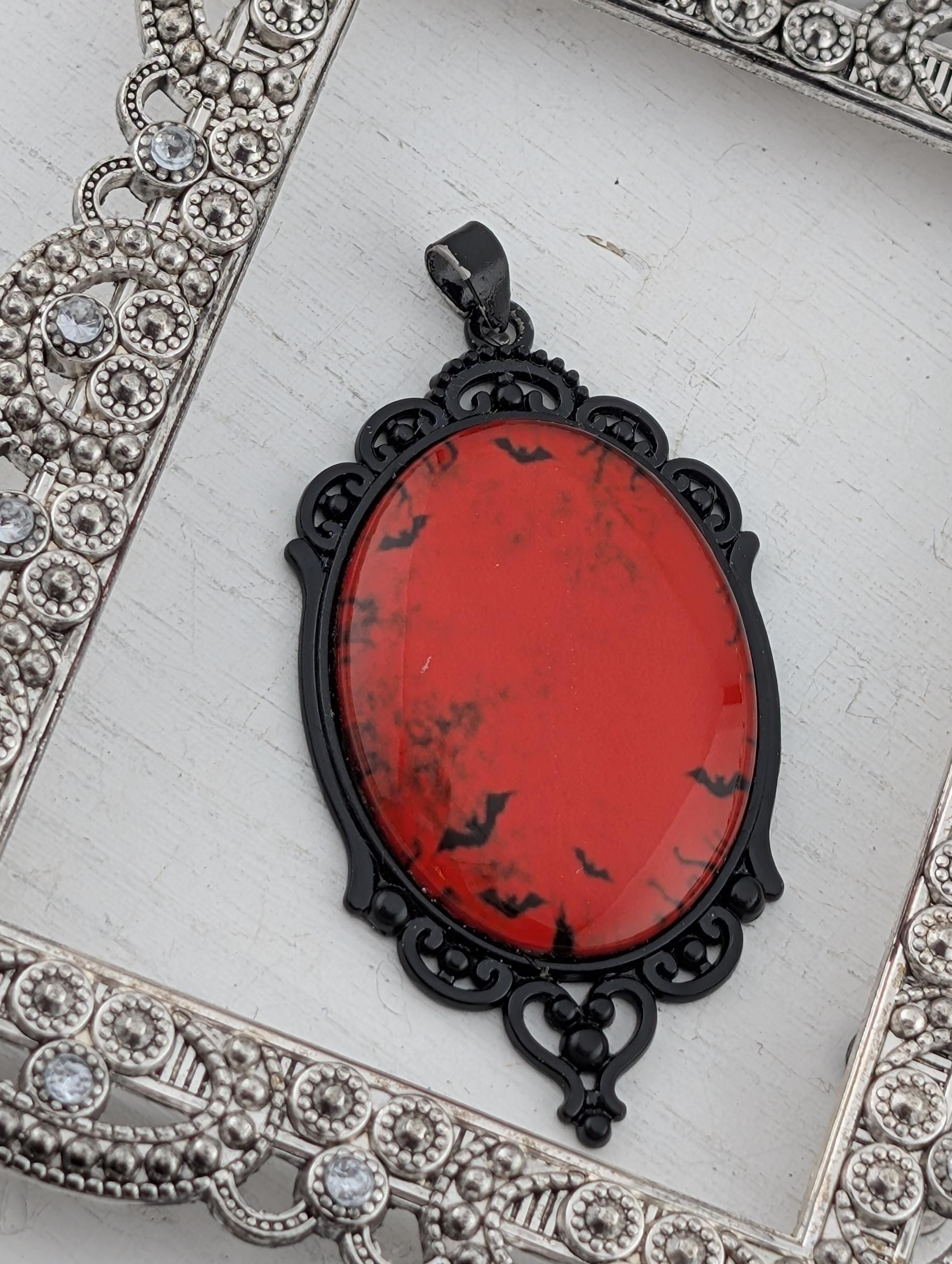 A red oval pendant with black bats on it, hanging from a black metal frame with an ornate design.