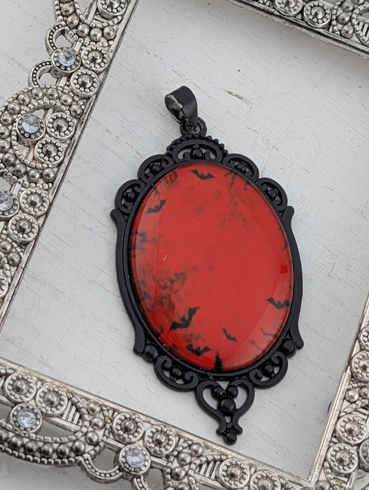 A red oval pendant with black bats on it, hanging from a black metal frame with an ornate design.