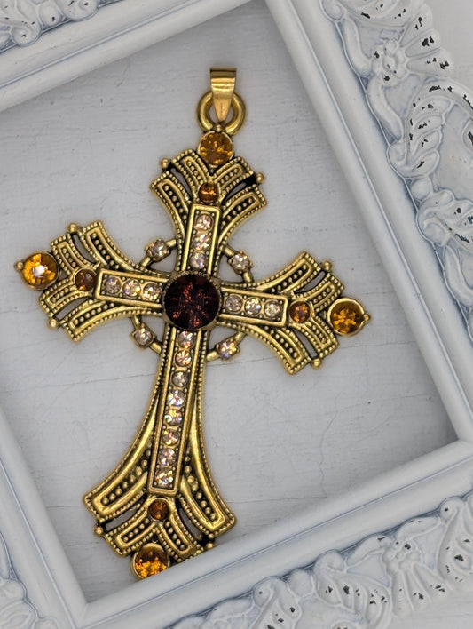 A decorative gold cross pendant with gemstones is displayed in a white ornate frame.