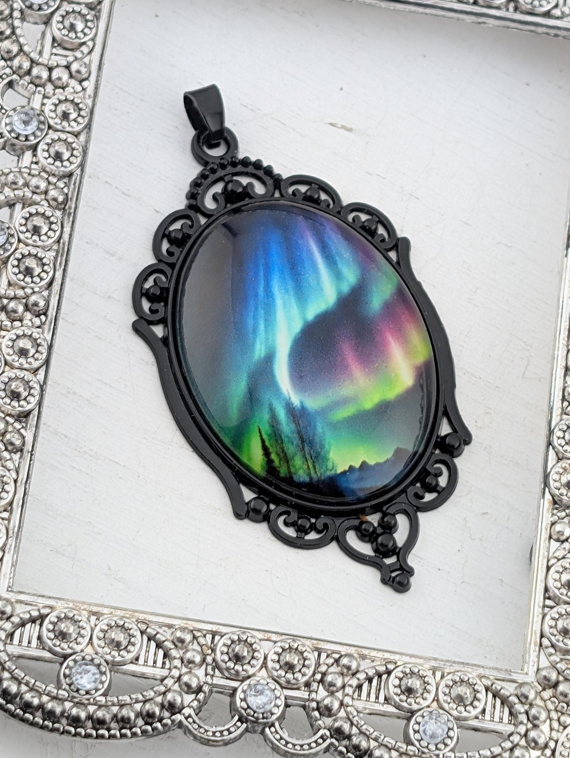 A pendant with a colorful, abstract design depicting a night sky with vibrant colors and patterns, such as the Aurora Borealis or Northern Lights.