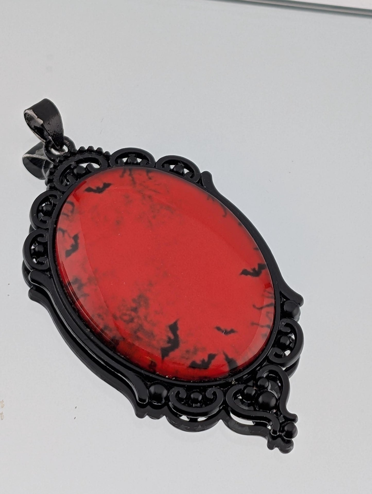 A red oval pendant with black bat silhouettes on it, hanging from a black metal frame with an ornate design.