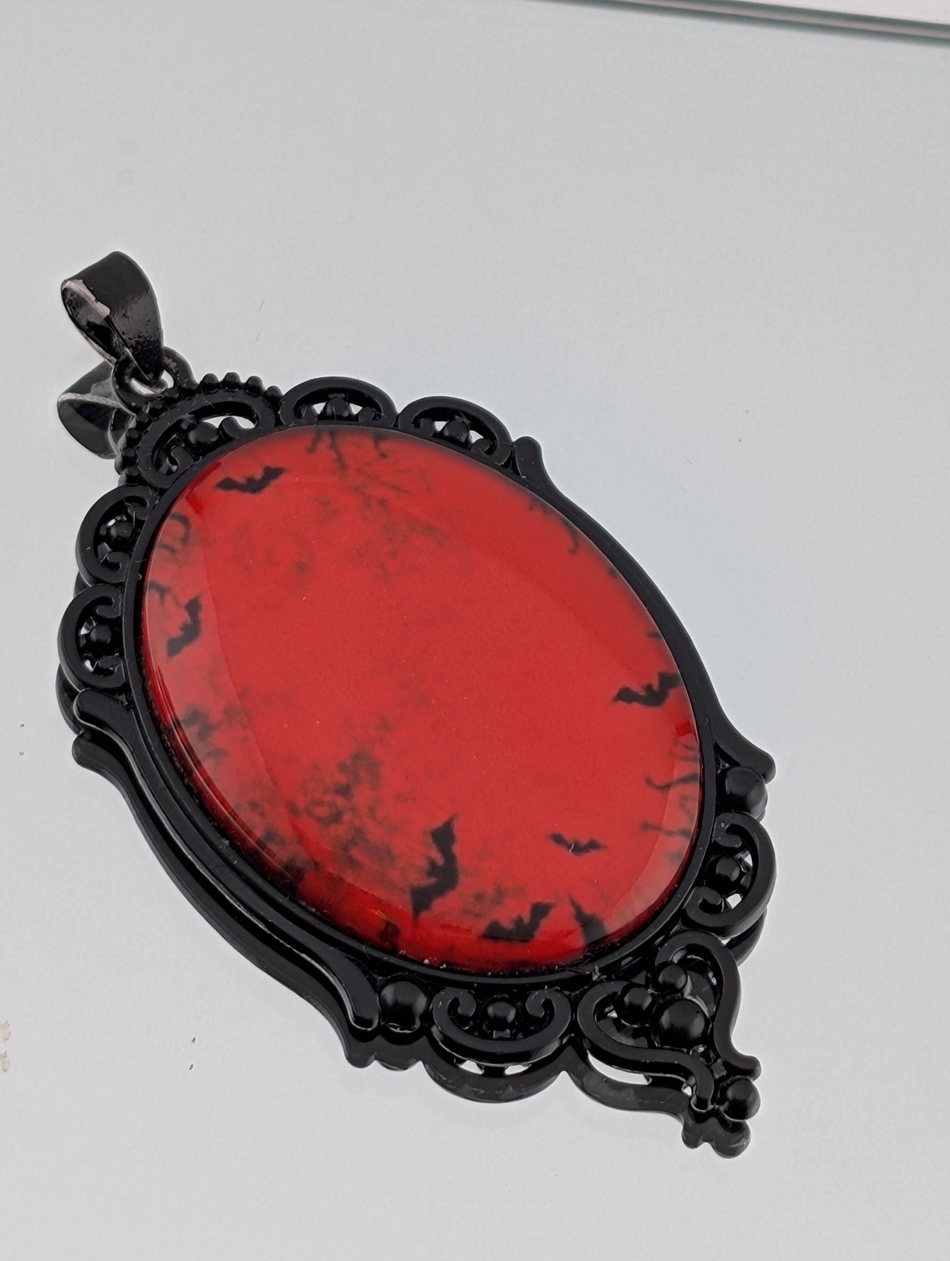 A red oval pendant with black bat silhouettes on it, hanging from a black metal frame with an ornate design.