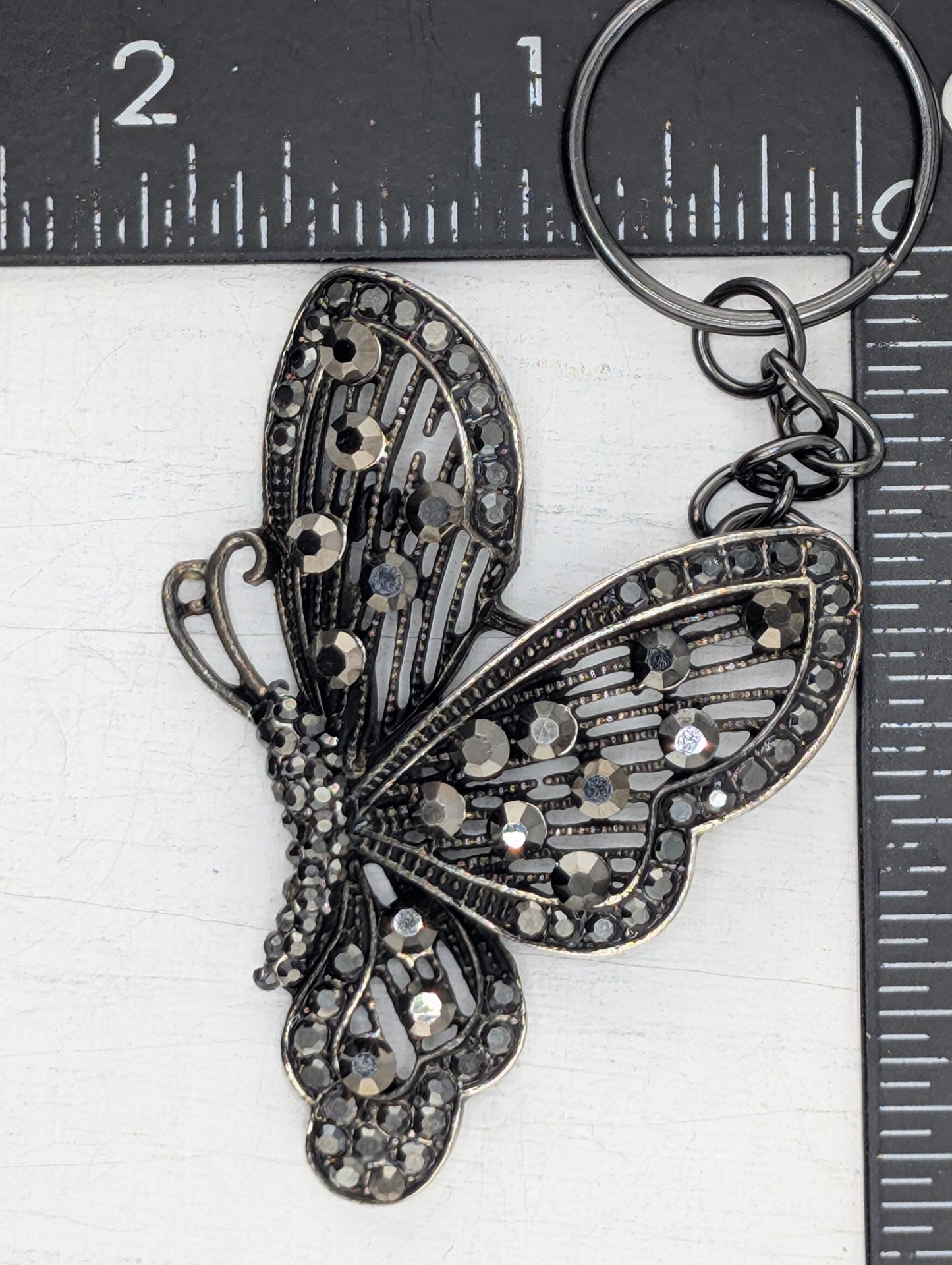 A decorative butterfly-shaped keychain with a metallic frame and sparkling rhinestones.
