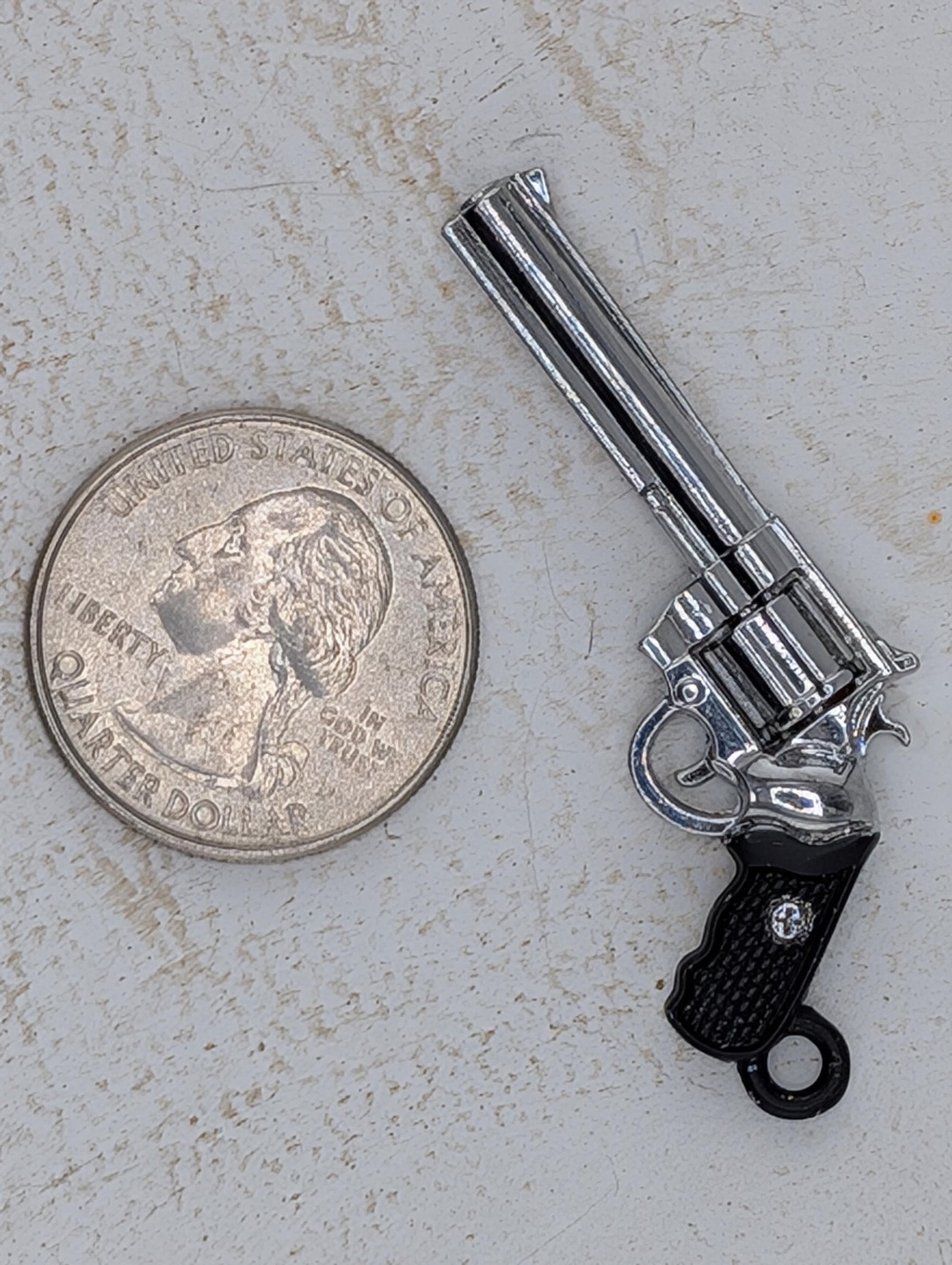 A toy silver-colored toy gun is placed next to a quarter on a white surface.