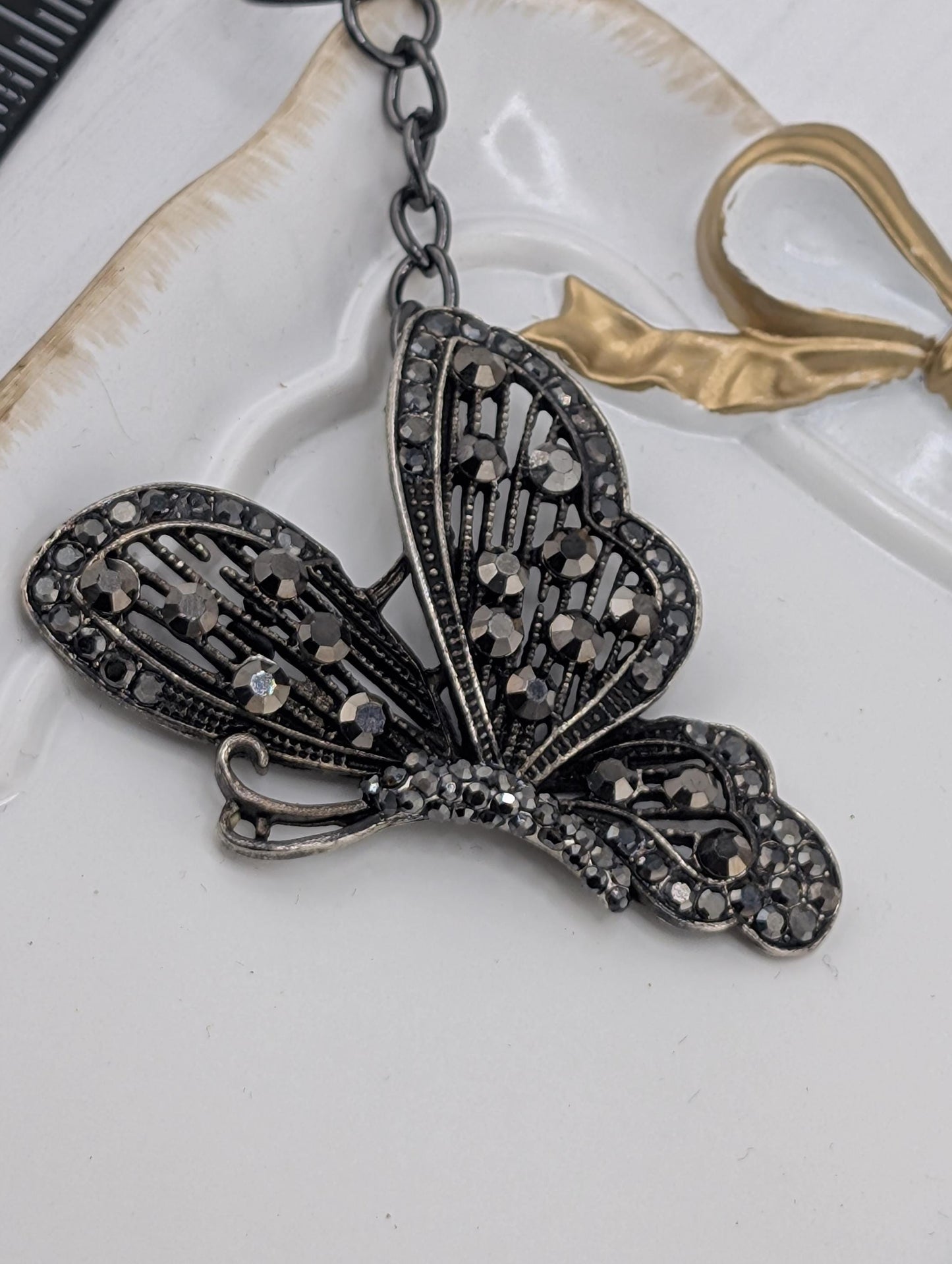 A decorative butterfly-shaped pendant with a black and silver design, featuring small rhinestones or crystals on its wings and body.