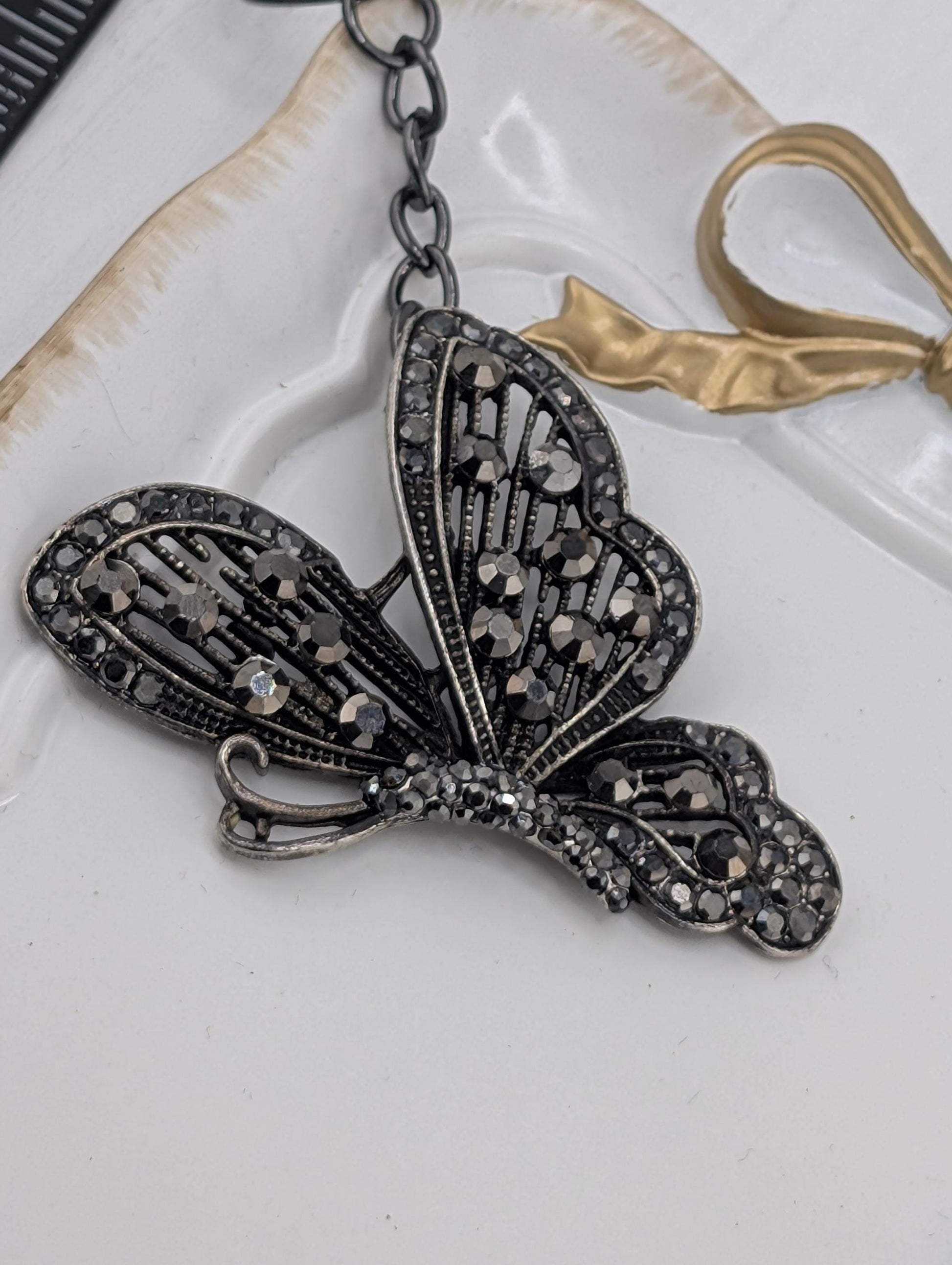 A decorative butterfly-shaped pendant with a black and silver design, featuring small rhinestones or crystals on its wings and body.