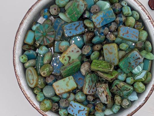 A bowl filled with various colorful beads, including green, blue, and brown ones, creating a vibrant and visually appealing display.