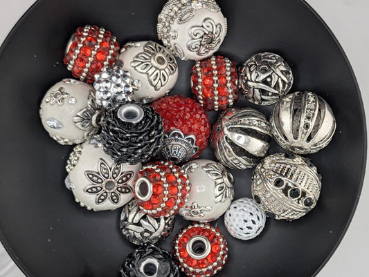 A black bowl filled with various decorative beads, including red, silver, and white beads, as well as some with intricate designs.