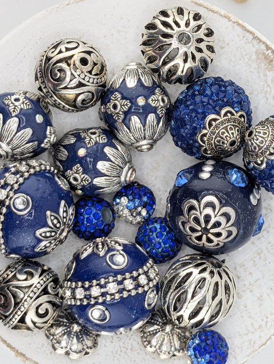 a collection of blue and silver beads, including various shapes and sizes, arranged on a white surface.