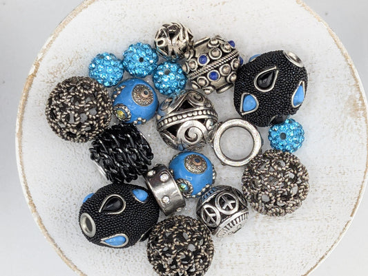 a collection of various beads and jewelry pieces, including black, silver, and blue elements, arranged on a white surface.
