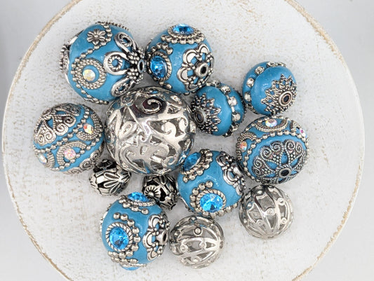 a collection of ornate, blue beads and metal beads arranged on a white surface.