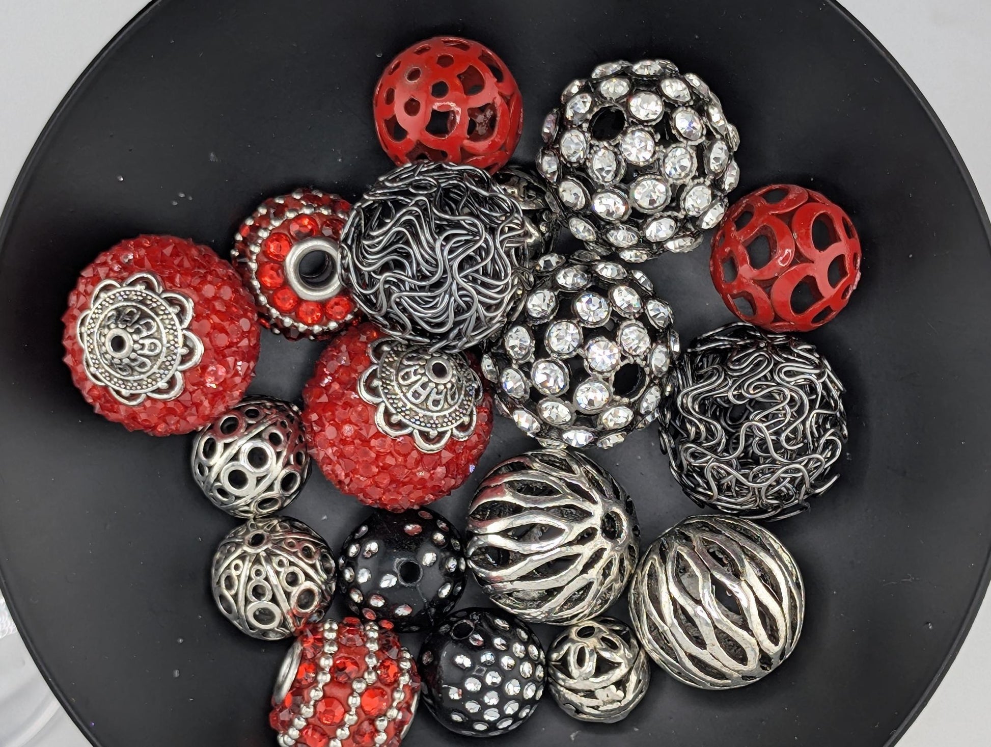 A black bowl filled with various beads and jewelry pieces, including red, silver, and black beads with intricate designs.