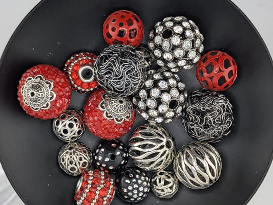 A black bowl filled with various beads and jewelry pieces, including red, silver, and black beads with intricate designs.