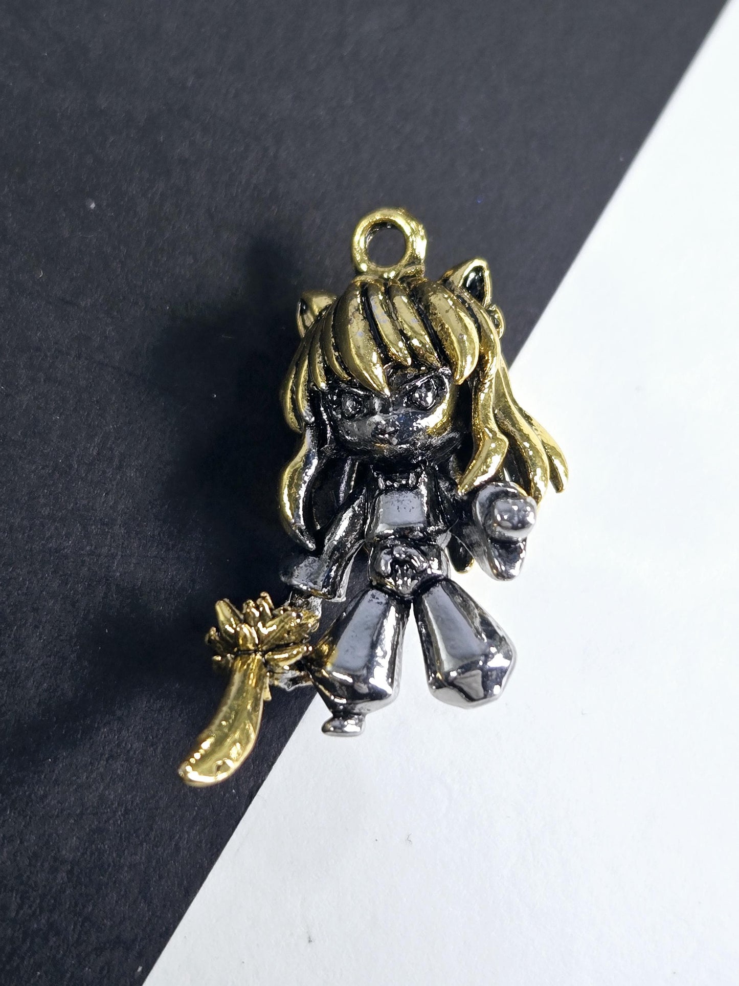 A decorative metal charm in the shape of a girl with a golden headband and a silver body, resting on a black surface.