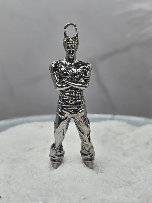 A silver-colored metal charm in the shape of a person, possibly a pendant or bracelet, is shown against a blurred background.