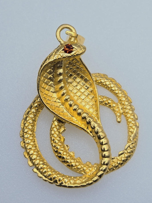 A gold-colored pendant in the shape of a snake, with a gemstone in its mouth.