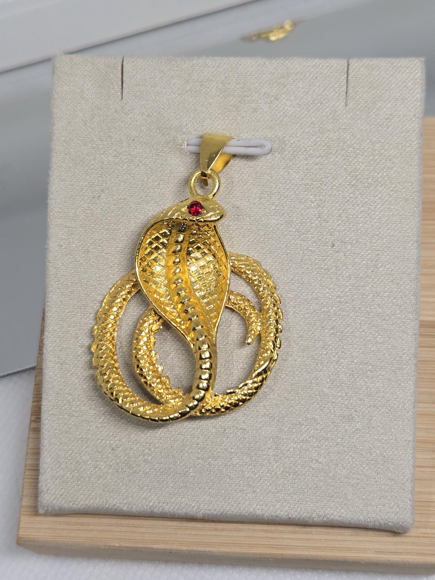 A gold snake pendant with a red gemstone is displayed on a white background.