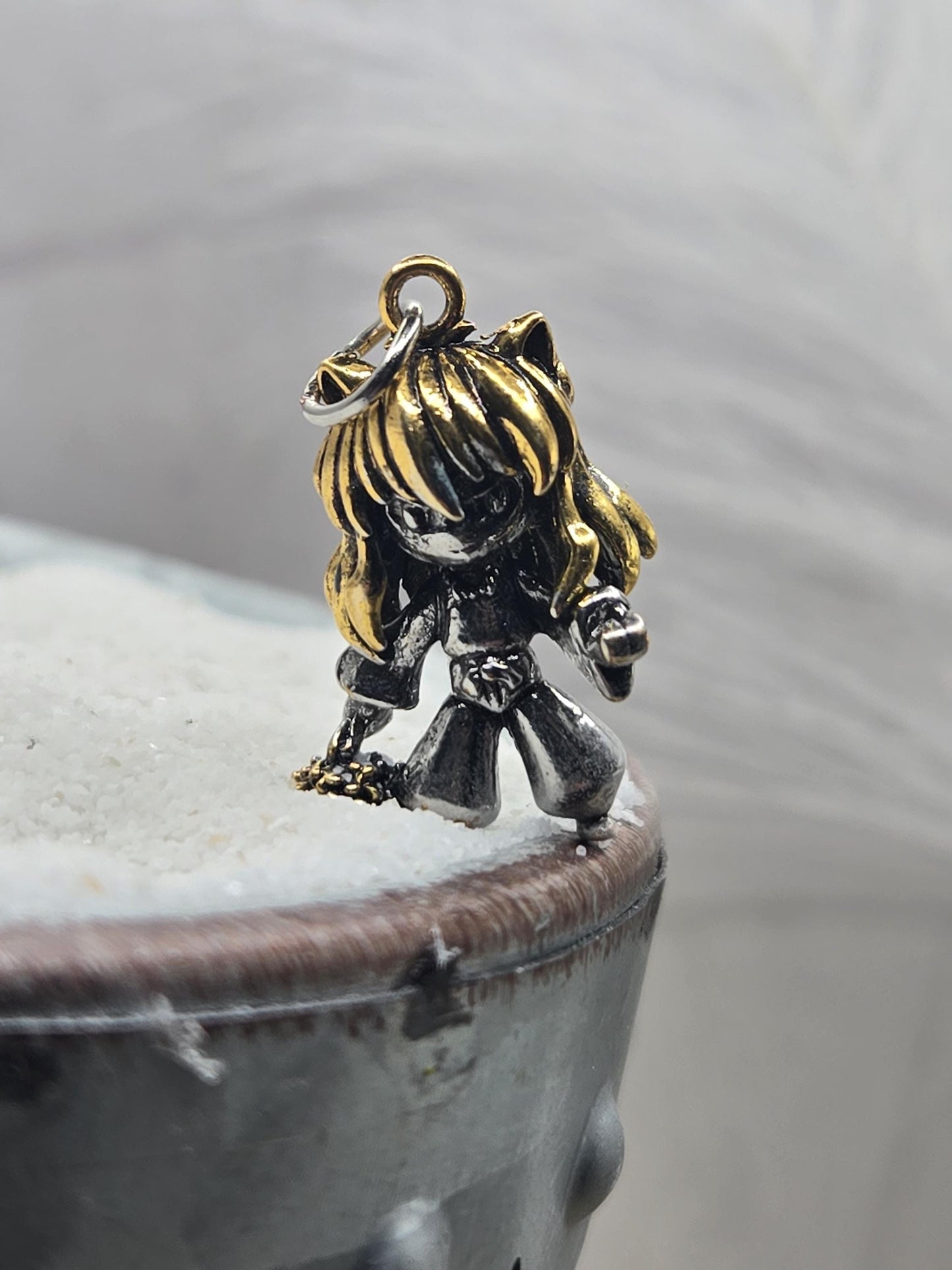 A close-up image of a decorative charm or pendant, featuring a metallic or gold-colored figure with a unique design.