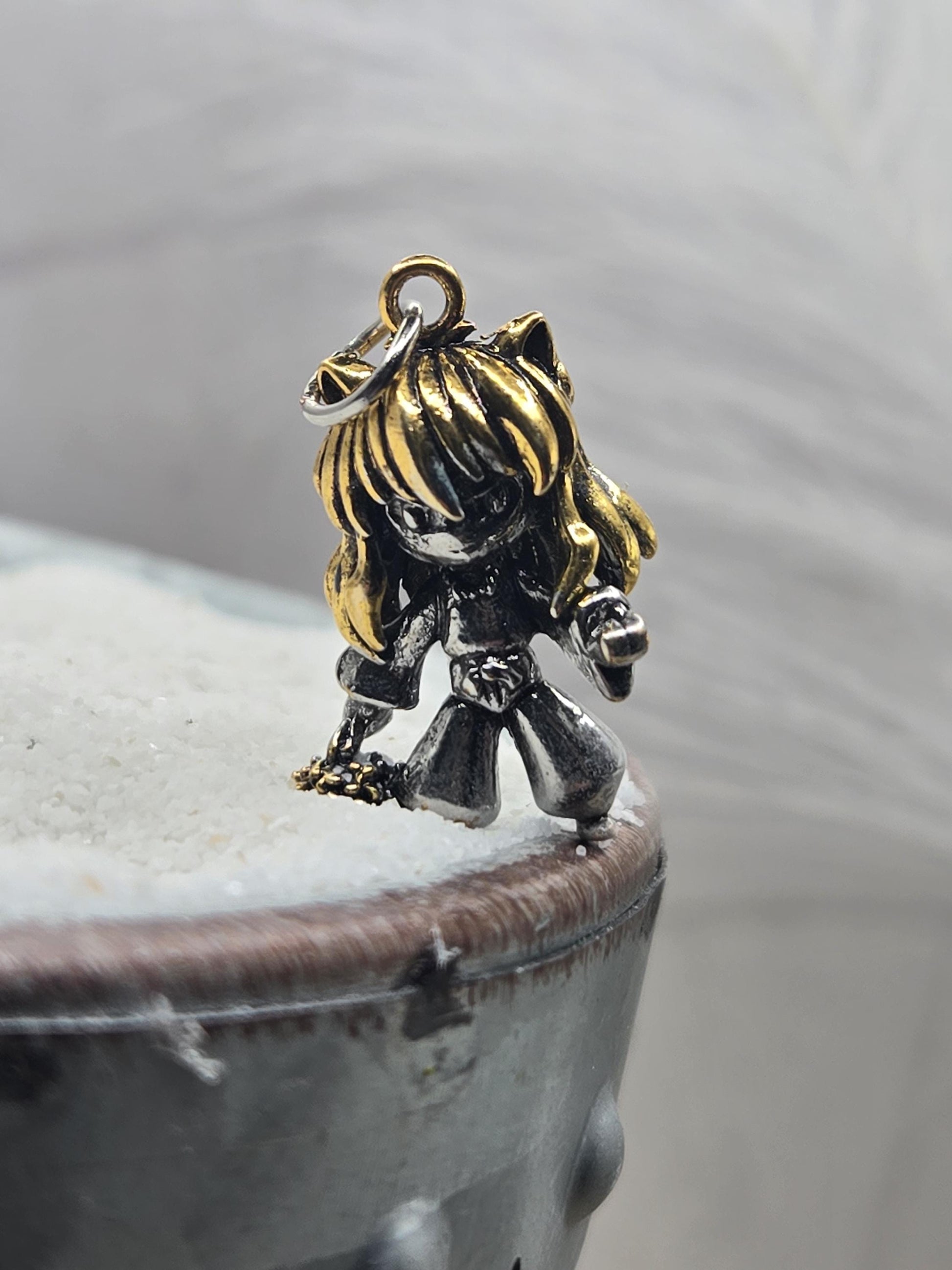 A close-up image of a decorative charm or pendant, featuring a metallic or gold-colored figure with a unique design.
