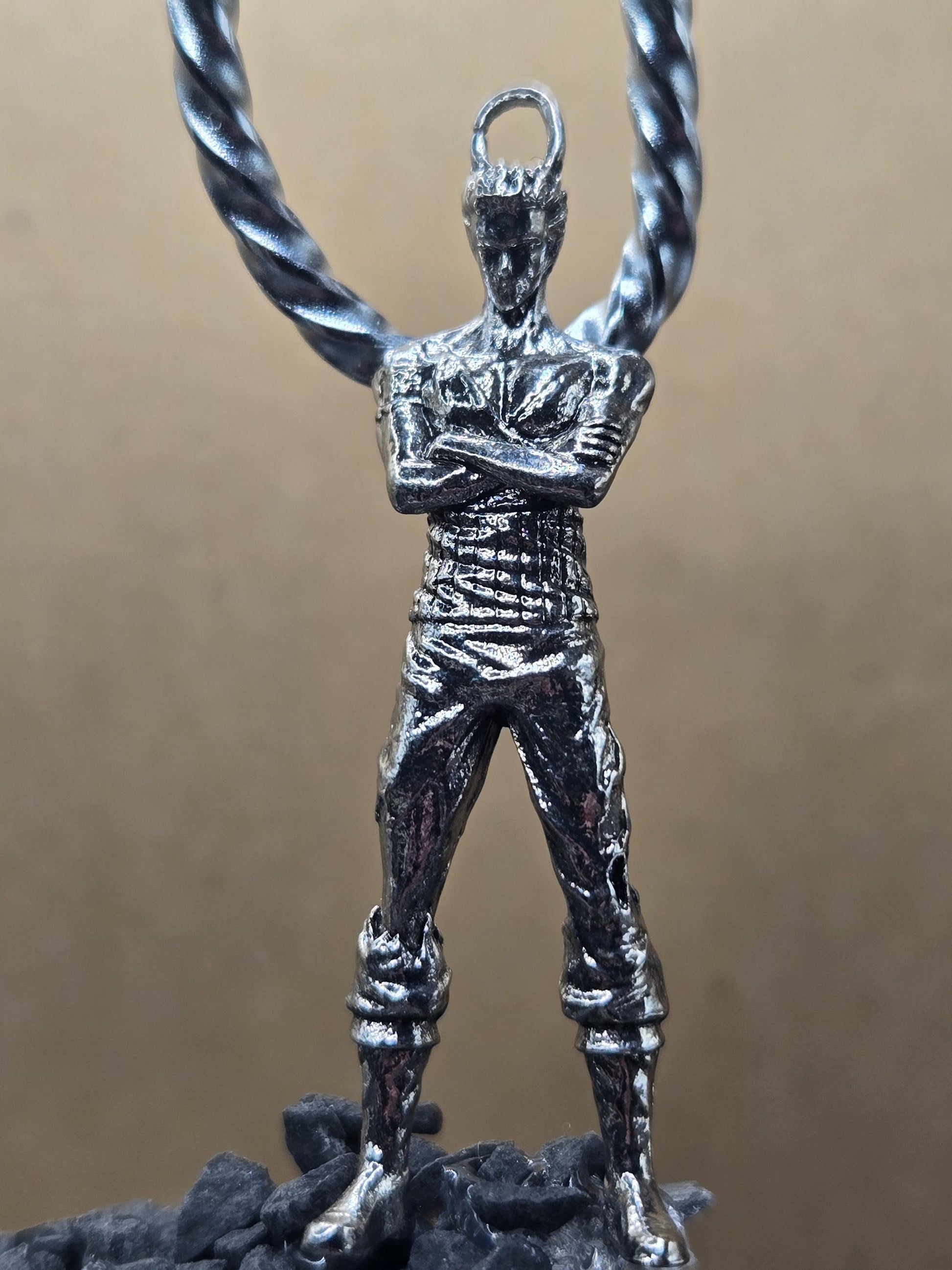 A close-up view of a silver-colored metal pendant or charm in the shape of a person, possibly a figure of a soldier or a character from a story or movie.