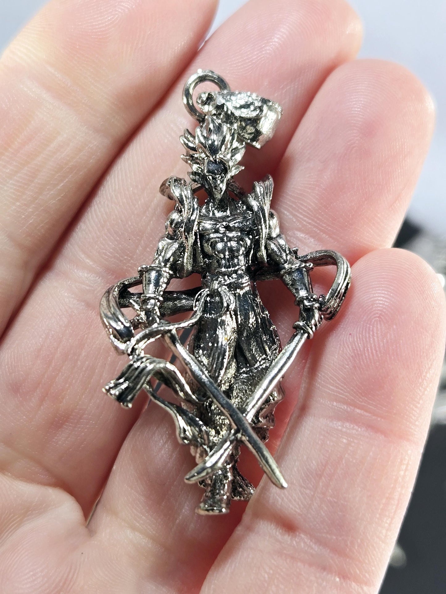 A close-up image of a person&#39;s hand holding a silver-colored metal pendant or brooch with an intricate design.