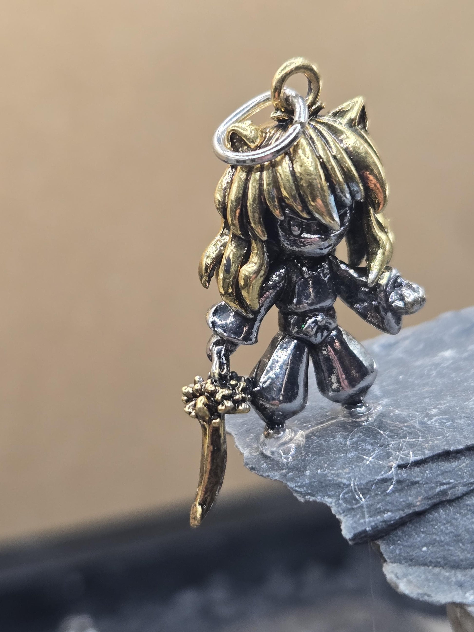 A close-up image of a decorative charm or pendant, featuring a metallic figure with a flowing, golden hair design.