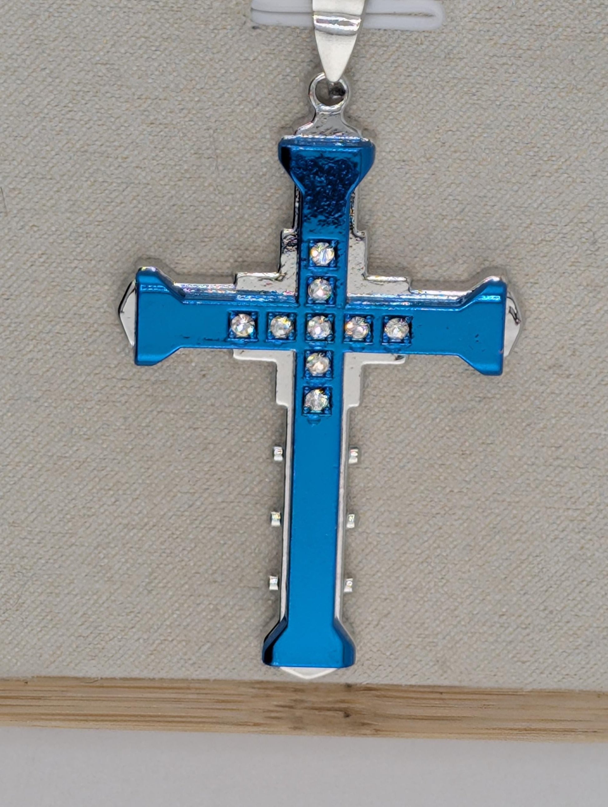 A blue and silver cross pendant with small rhinestones or crystals on it, hanging from a chain.
