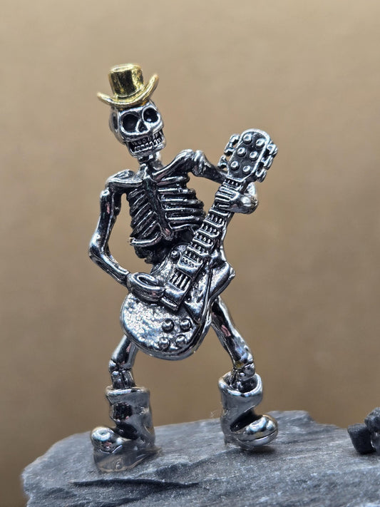 A metal figurine of a skeleton playing a guitar.