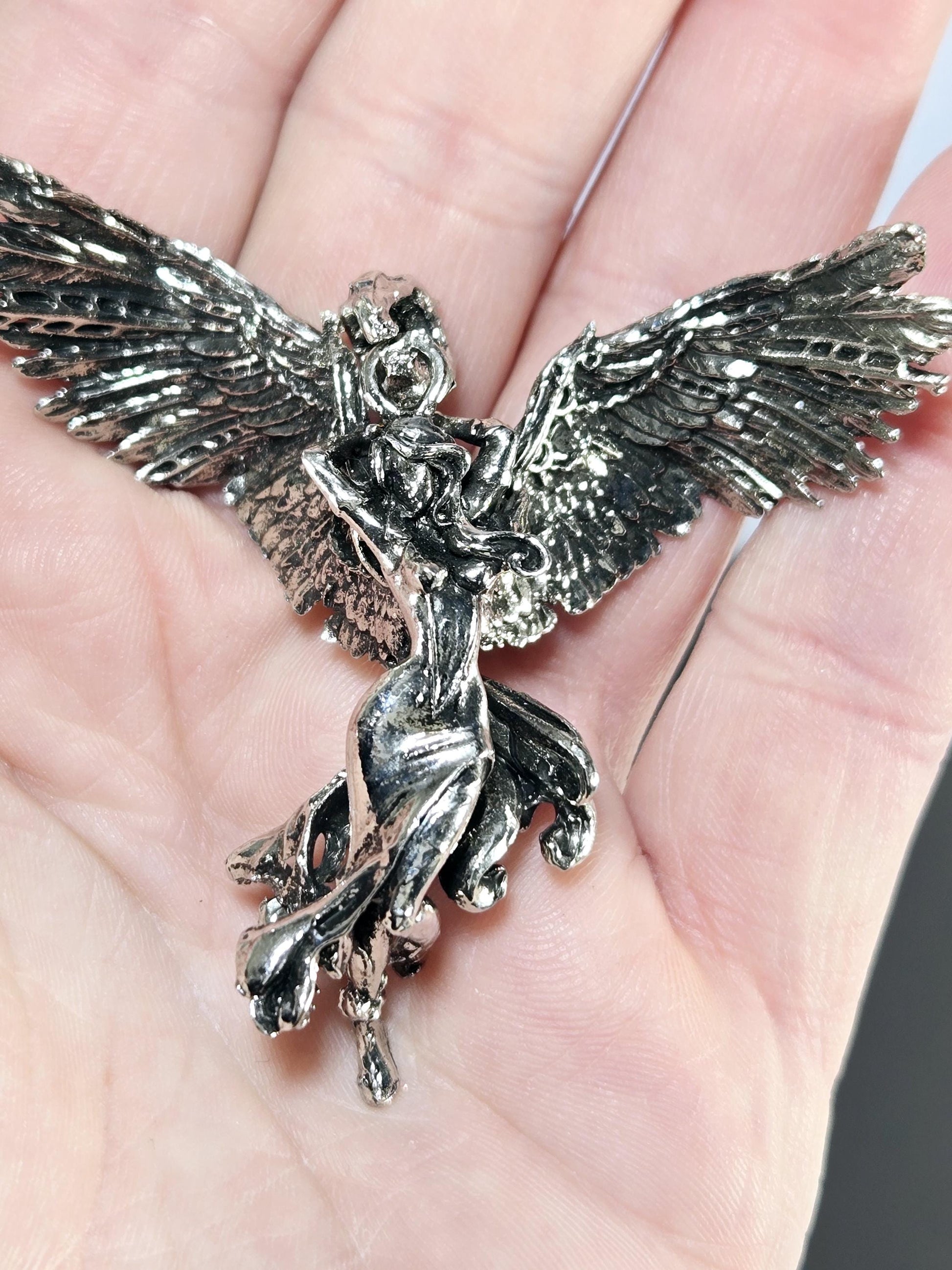 A close-up image of a person&#39;s hand holding a silver-colored metal sculpture of a bird or winged creature.