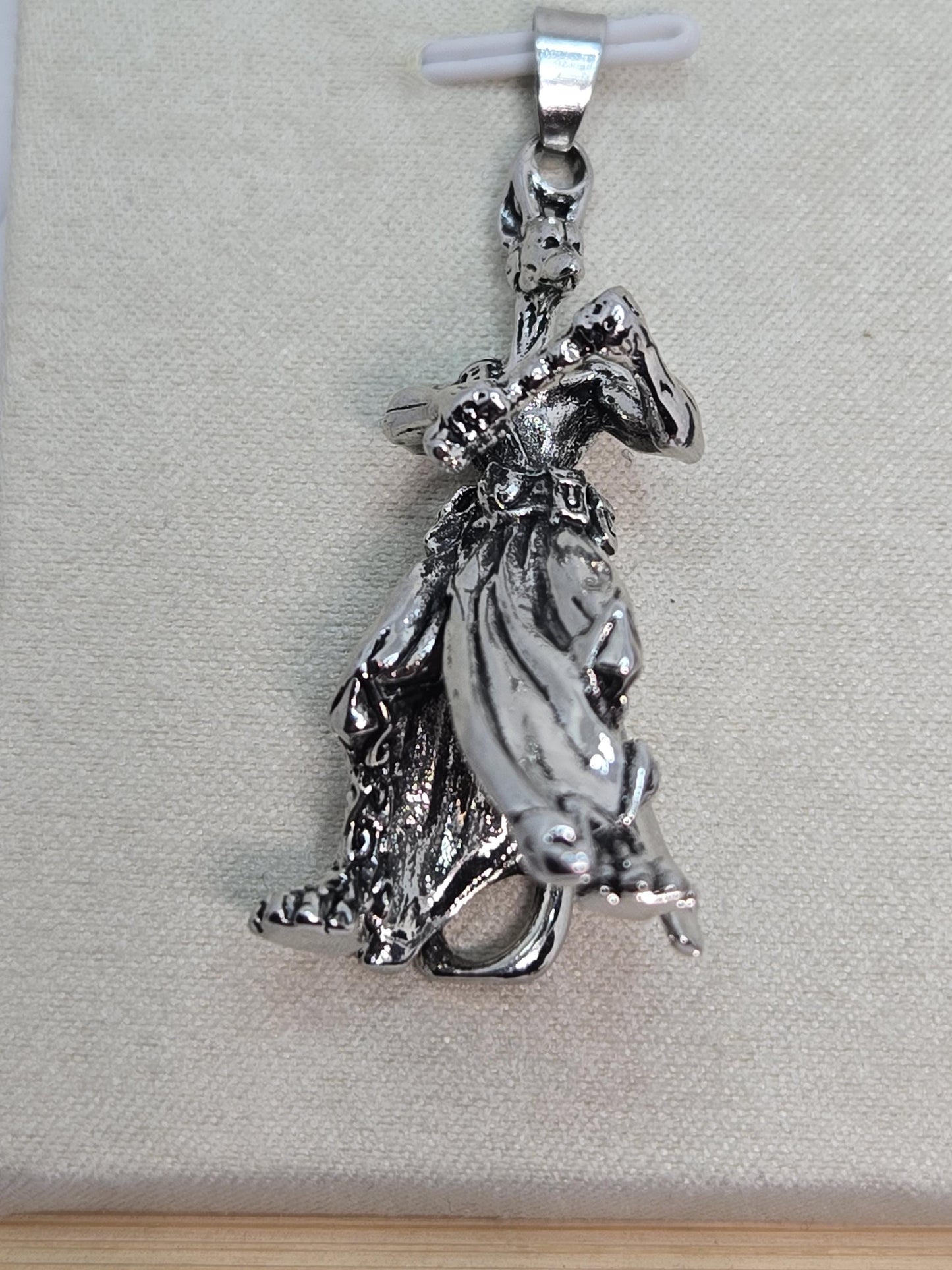 A silver-colored metal charm or pendant in the shape of a bird or a winged creature, resting on a textured surface.