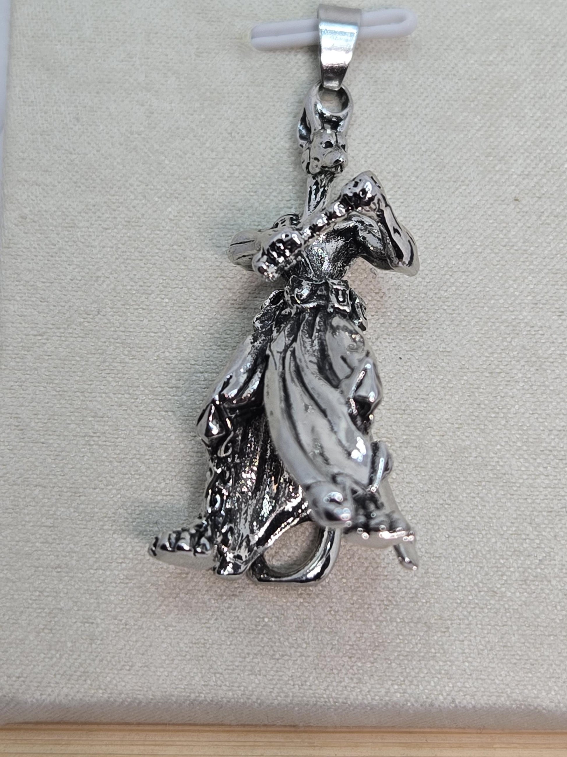 A silver-colored metal charm or pendant in the shape of a bird or a winged creature, resting on a textured surface.