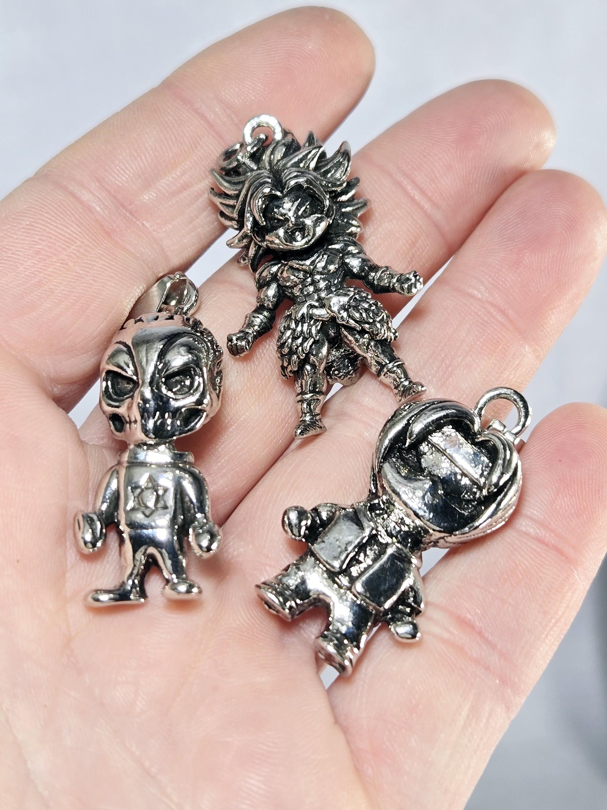 A hand holding four silver-colored charms, including a lion, a person, and two other figures.