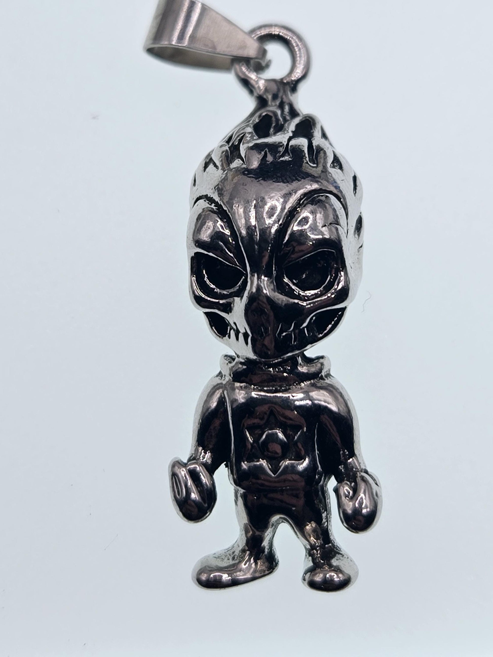 A silver-colored metal charm or pendant in the shape of a skull or alien-like figure.