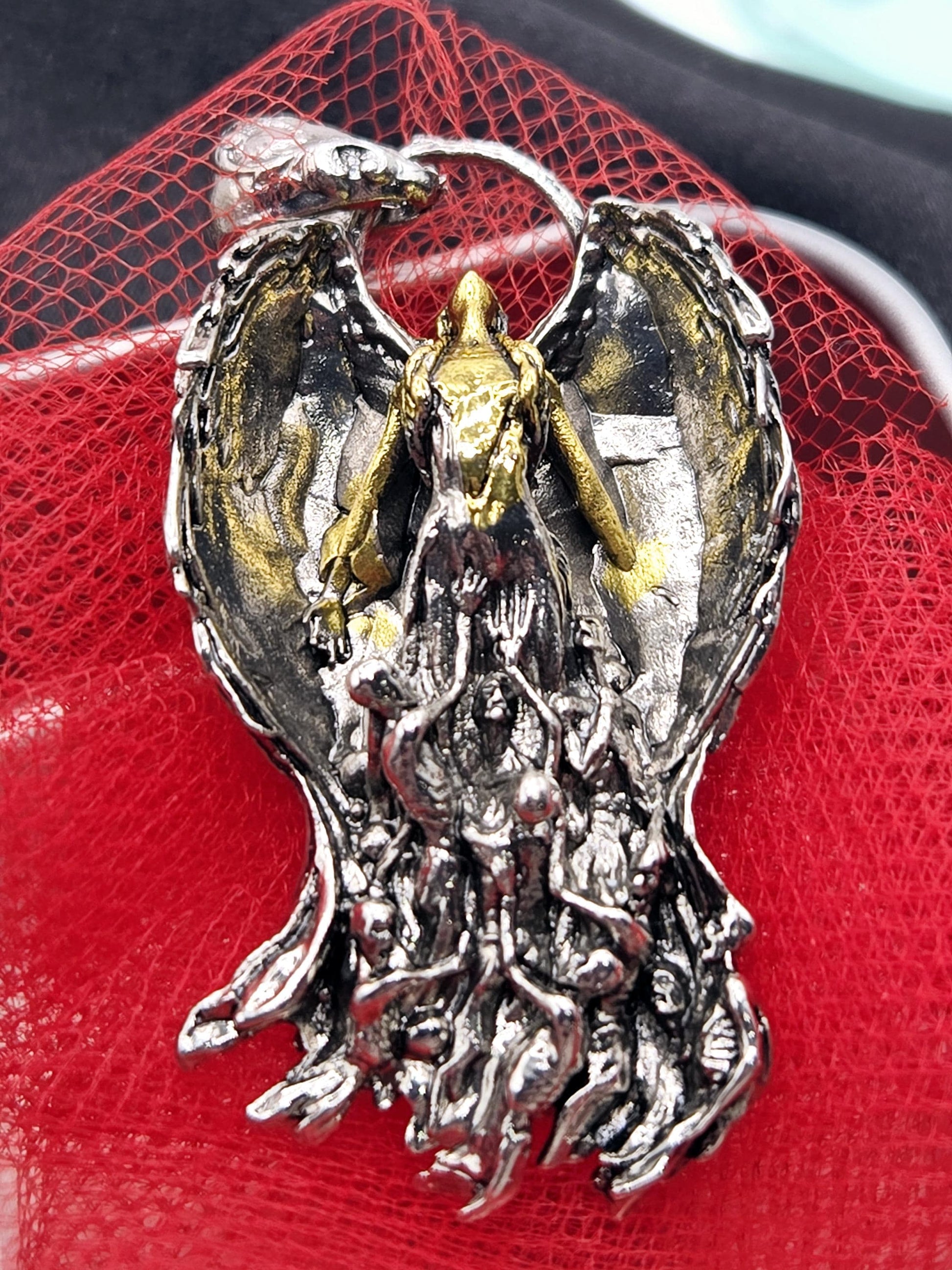 a close-up view of a decorative metal piece, possibly a pendant or brooch, with a red background.