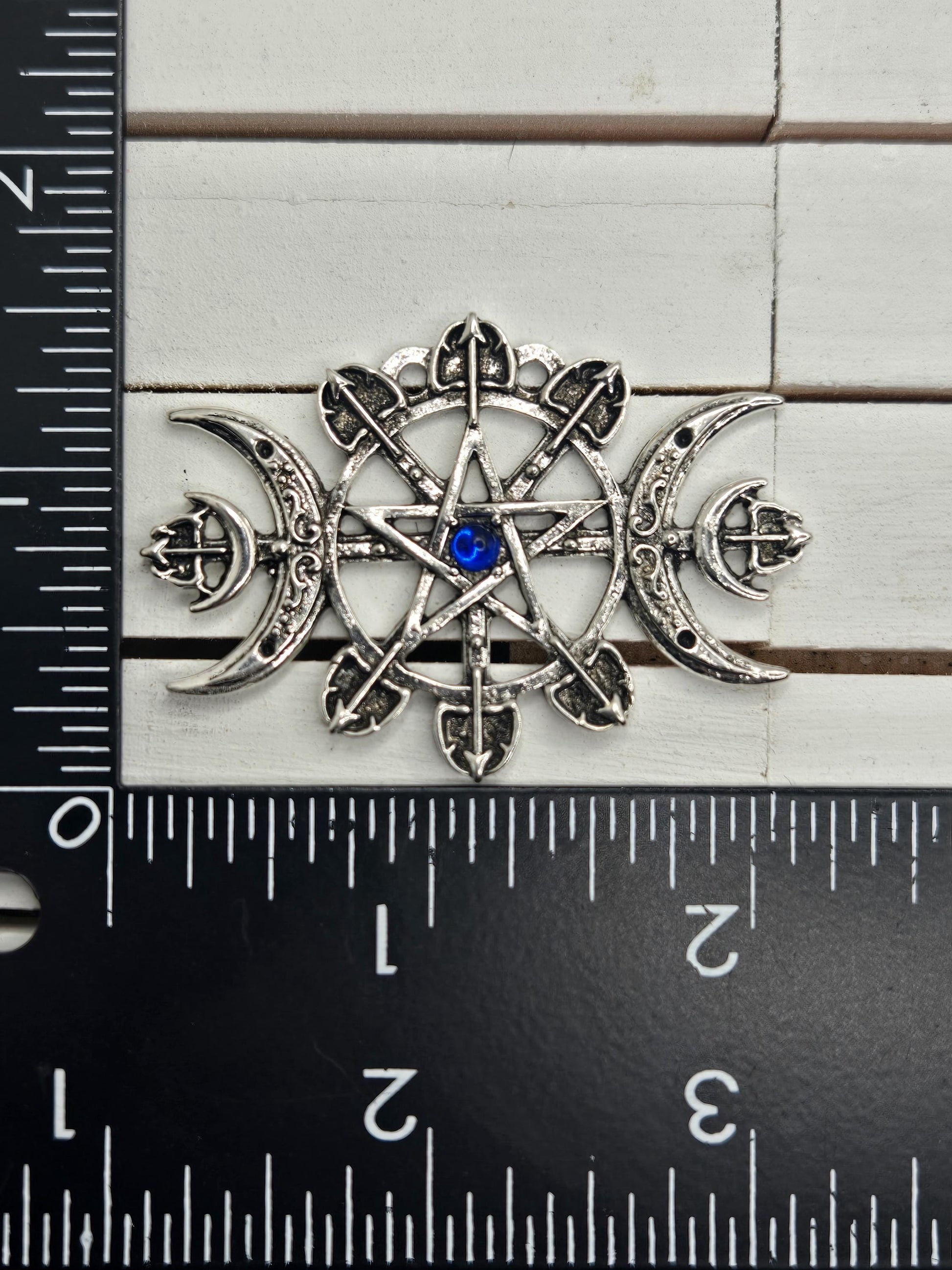 A silver-colored metal pin with a blue gemstone, placed next to a ruler for size comparison.