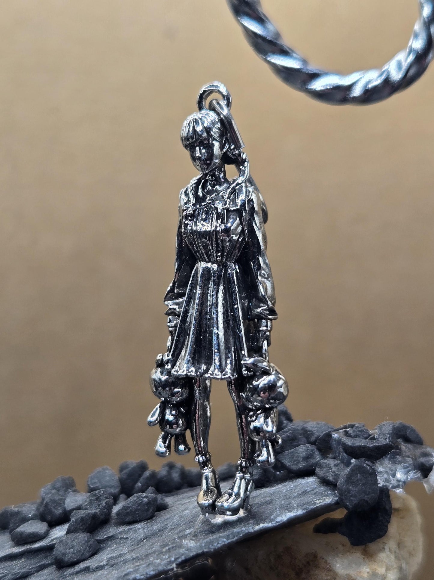 A silver-colored metal charm or pendant in the shape of a person, possibly a religious figure, is shown in the image.