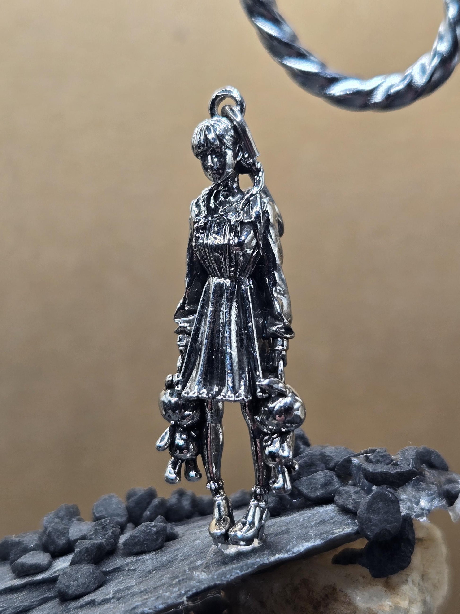 A silver-colored metal charm or pendant in the shape of a person, possibly a religious figure, is shown in the image.