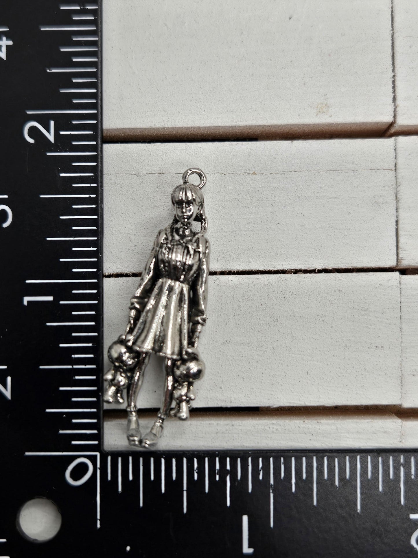 A silver-colored charm or pendant is placed next to a ruler on a white surface.