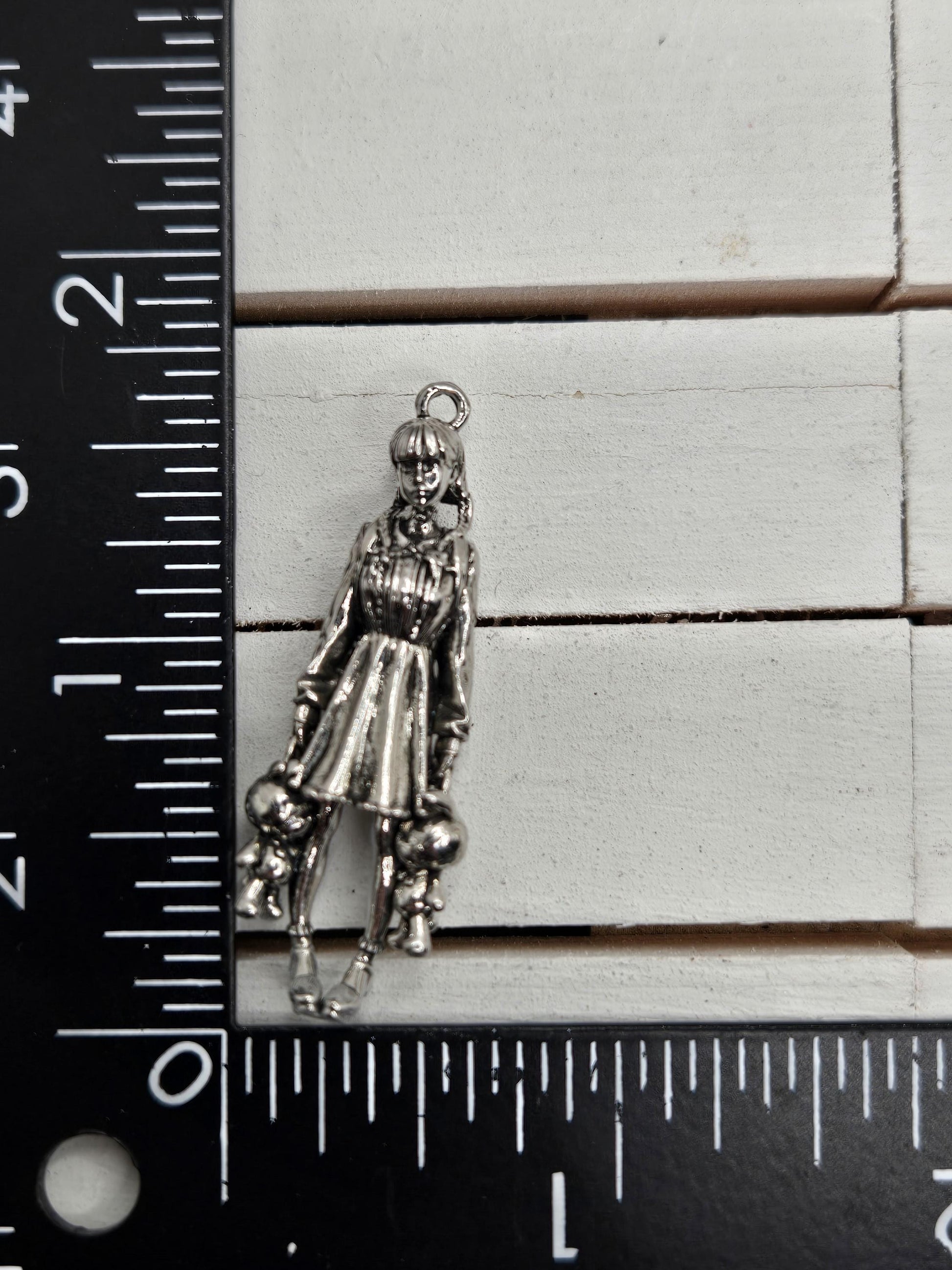 A silver-colored charm or pendant is placed next to a ruler on a white surface.