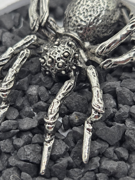 A close-up view of a metallic, spider-like object with intricate details, resting on a bed of small, dark rocks.