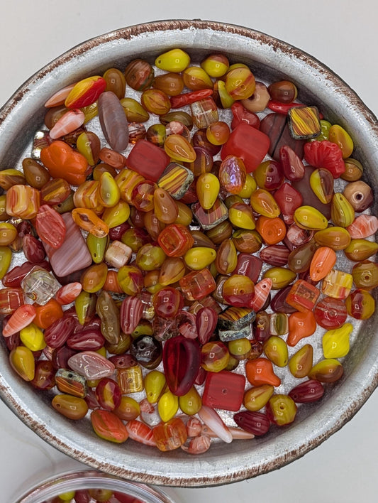 A bowl filled with a variety of colorful beads, including red, orange, yellow, and green beads, creating a vibrant and visually appealing display.