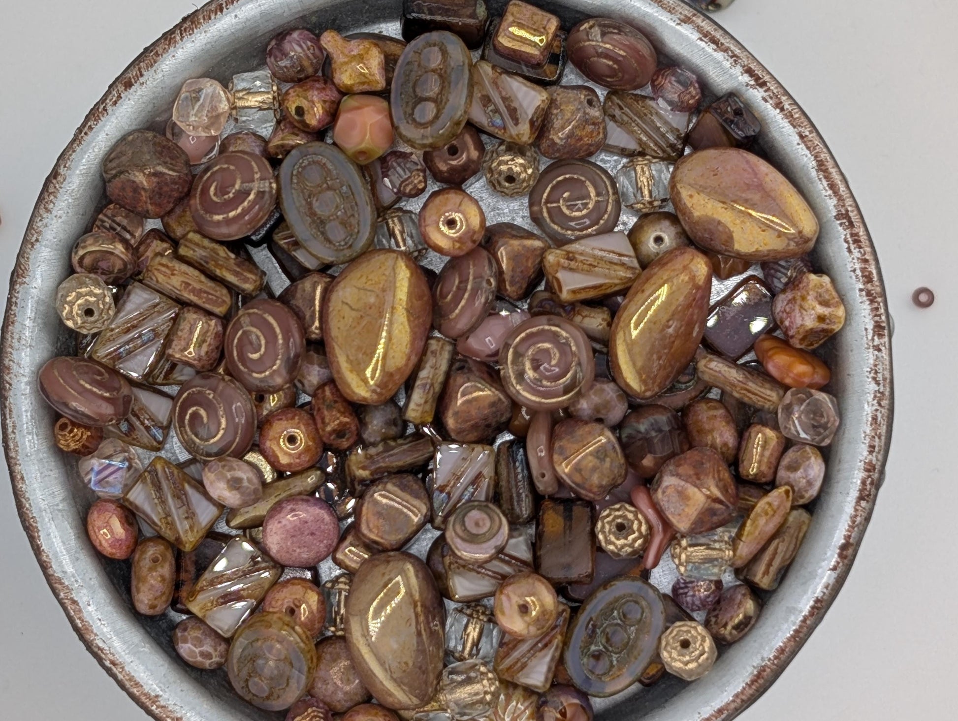 A bowl filled with various beads and stones of different shapes, sizes, and colors.