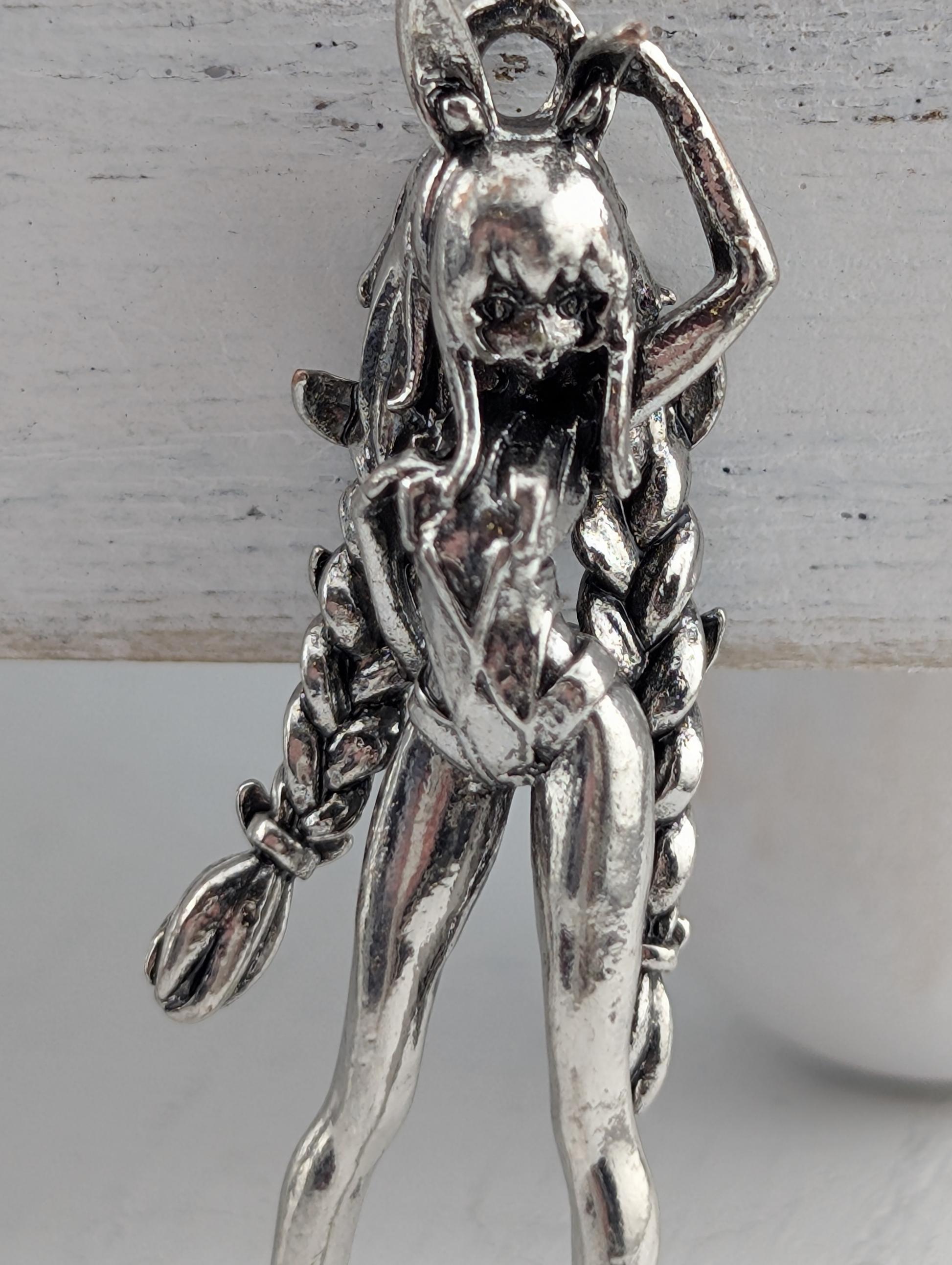 A silver-colored metal pendant in the shape of a female figure with long braided hair.