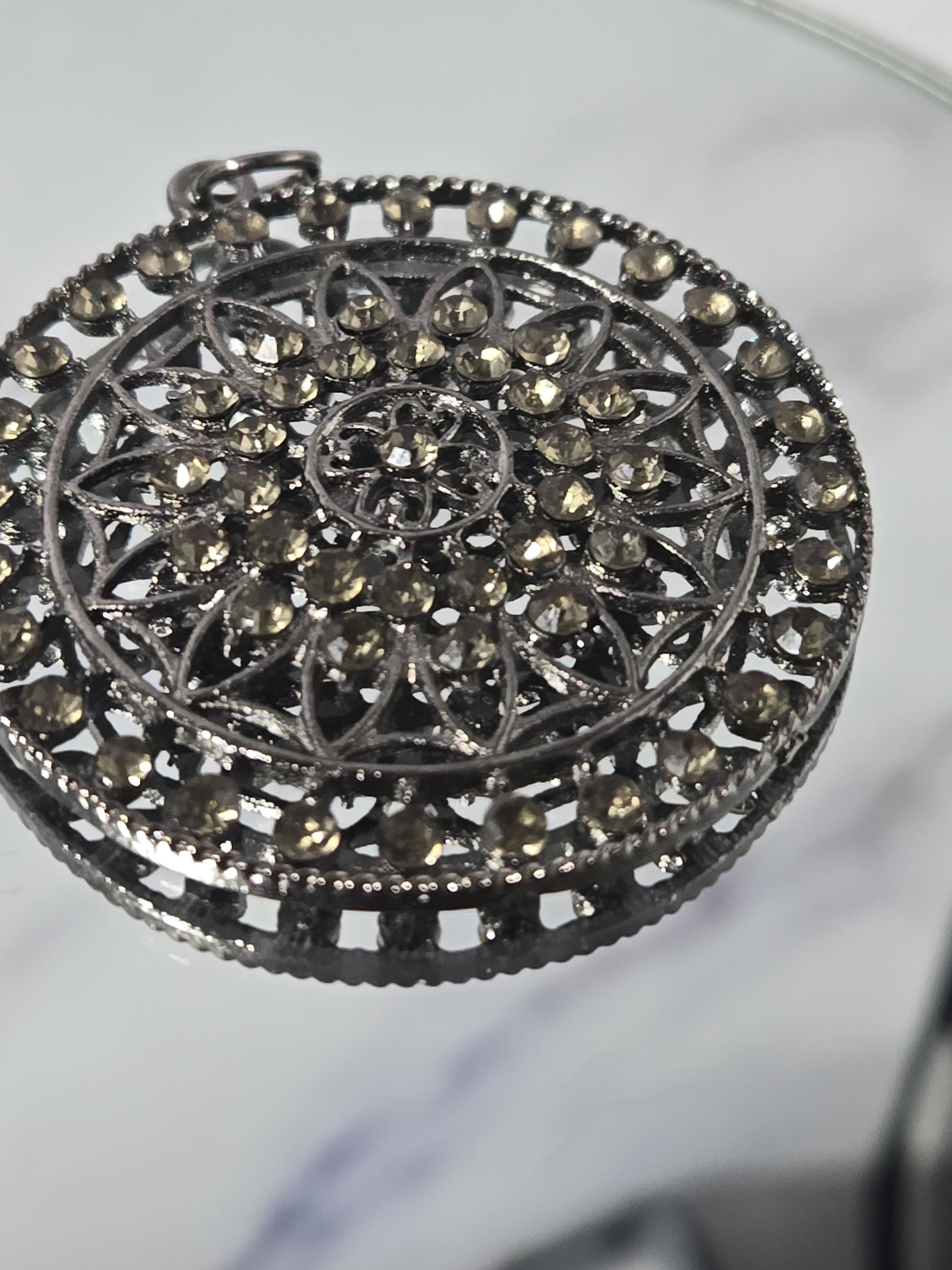 A close-up view of a decorative metal piece with a floral pattern and numerous small, round, and shiny stones or crystals embedded in it.
