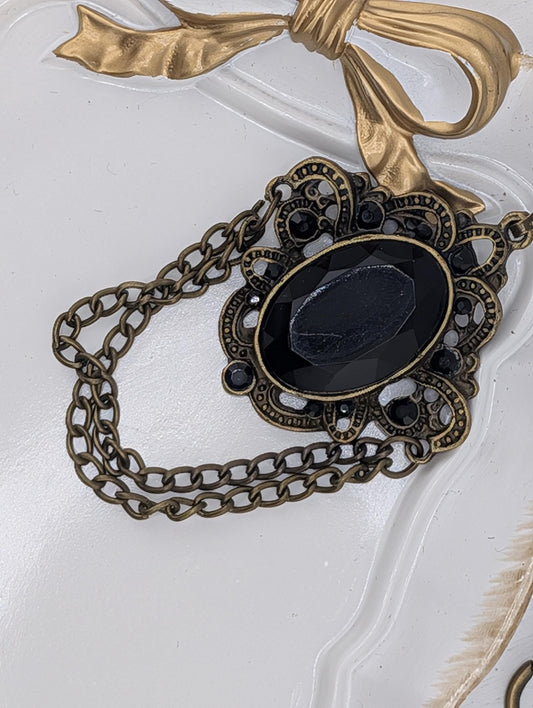 a close-up view of a decorative piece with a black gemstone and a gold chain.