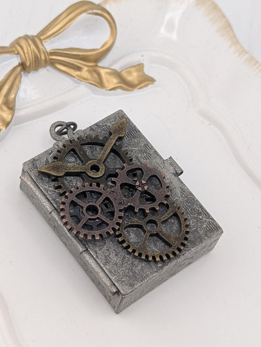 A metal pendant with gears and a ribbon is displayed on a white surface.