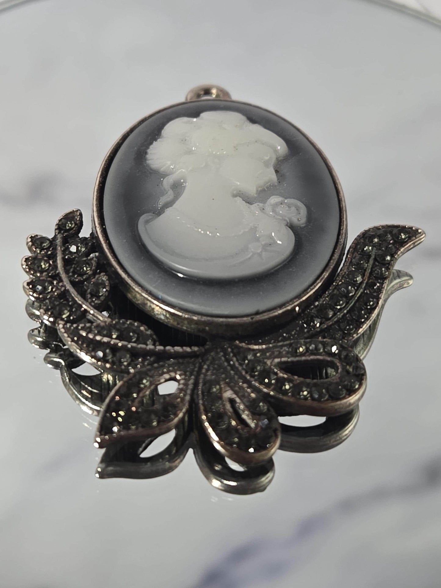 A decorative brooch with a white stone or gemstone in the center, surrounded by intricate metalwork and embellishments.