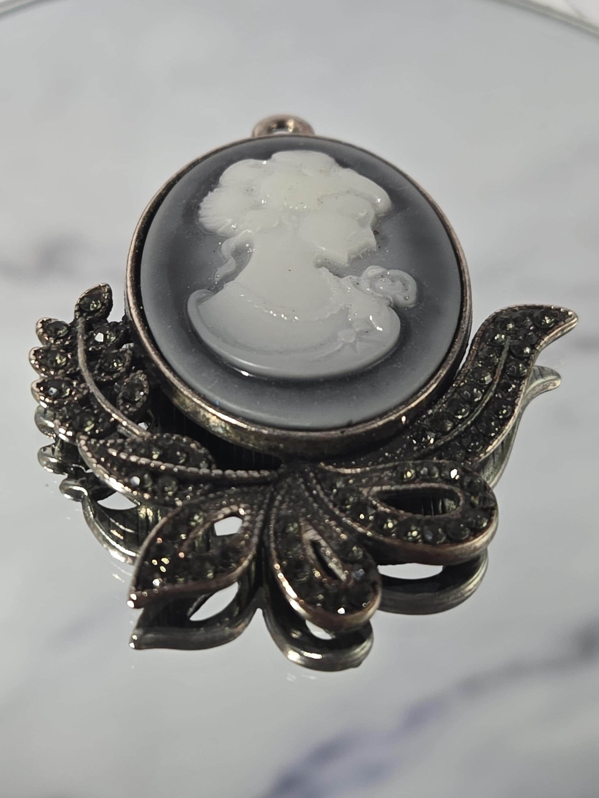 A decorative brooch with a white stone or gemstone in the center, surrounded by intricate metalwork and embellishments.