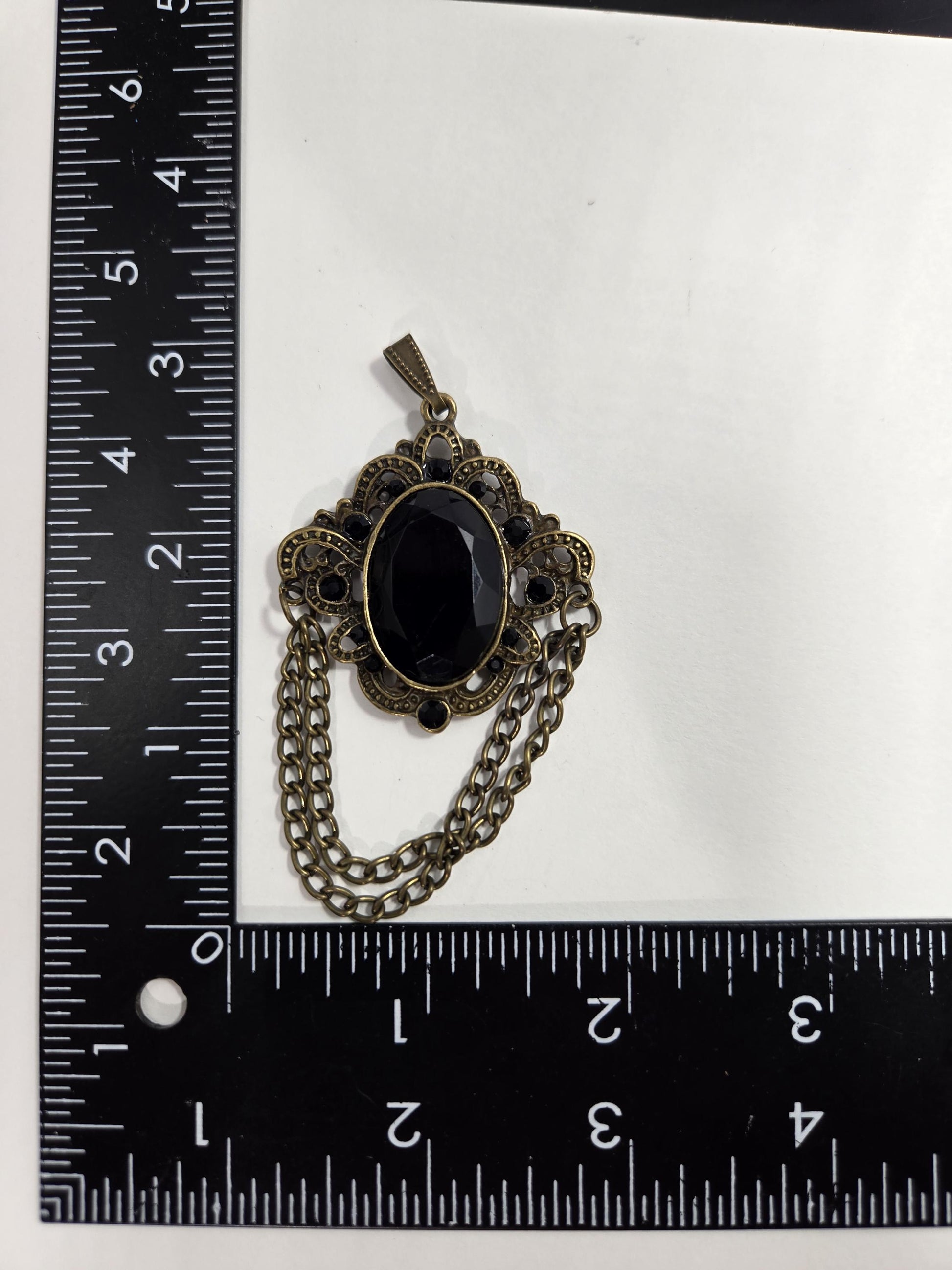 a black stone pendant with a decorative metal chain attached to it, placed on a ruler for size comparison.